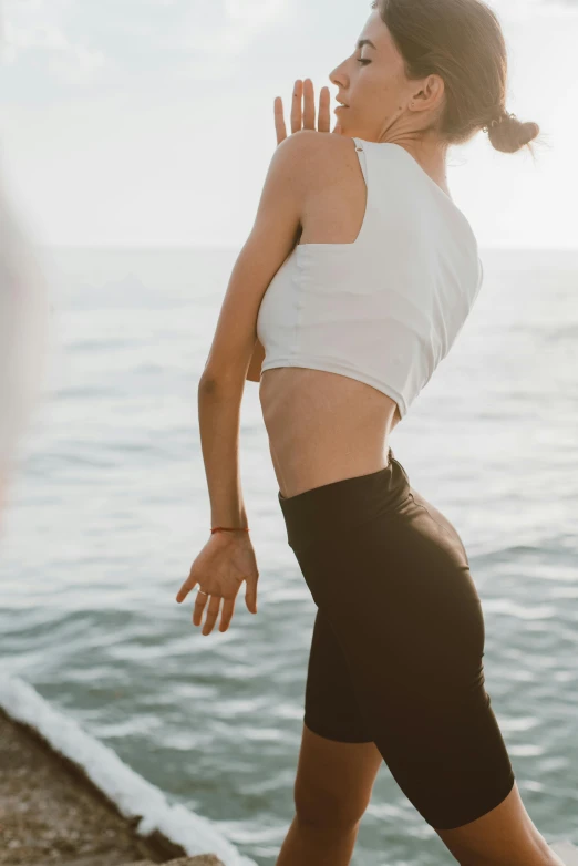 a woman running on a beach next to the ocean, trending on pexels, renaissance, wearing a sexy cropped top, thoughtful pose, close-up shot from behind, white tank top