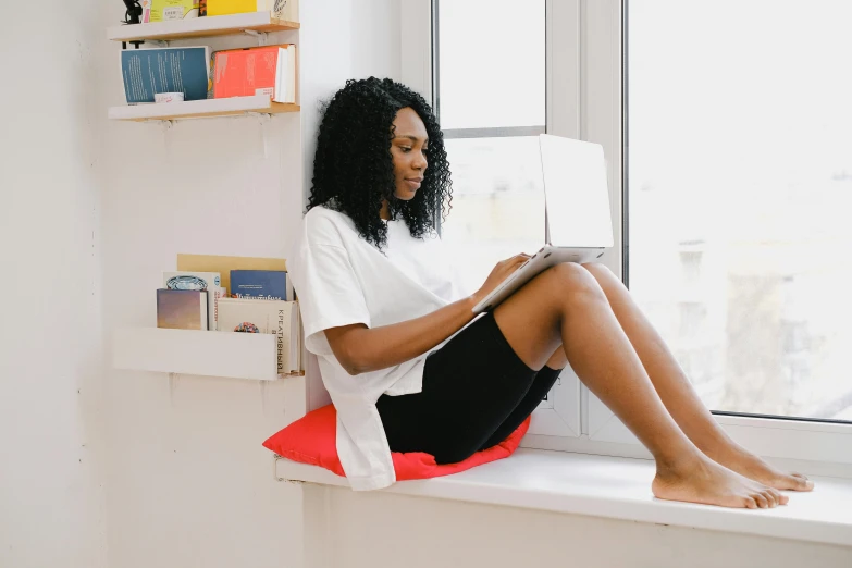 a woman sitting on a window sill using a laptop, pexels contest winner, happening, black woman, dressed in a white t shirt, sitting on a red button, reading nook