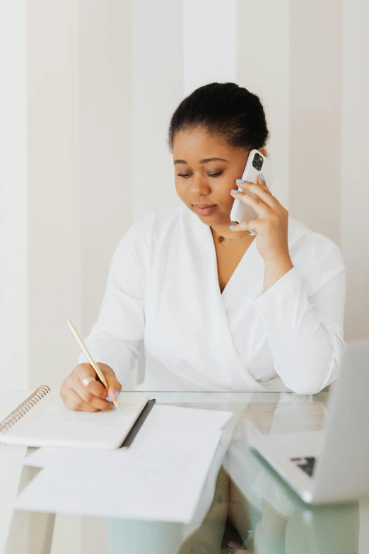 a woman sitting at a desk talking on a cell phone, white and gold color scheme, writing on a clipboard, african american woman, slightly minimal