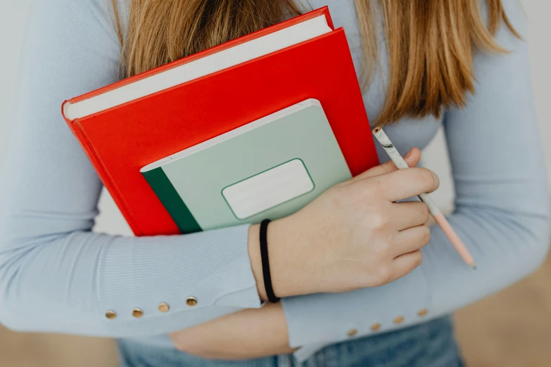 a close up of a person holding a book and a pencil, an album cover, by Emma Andijewska, pexels contest winner, blue and red, holding books, teenage female schoolgirl, 15081959 21121991 01012000 4k