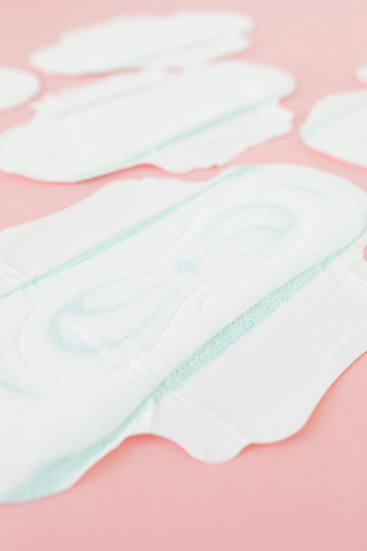 a pair of sanitary pads sitting on top of a pink surface, detailed shot legs-up, detailed product image, in a row, cartouche