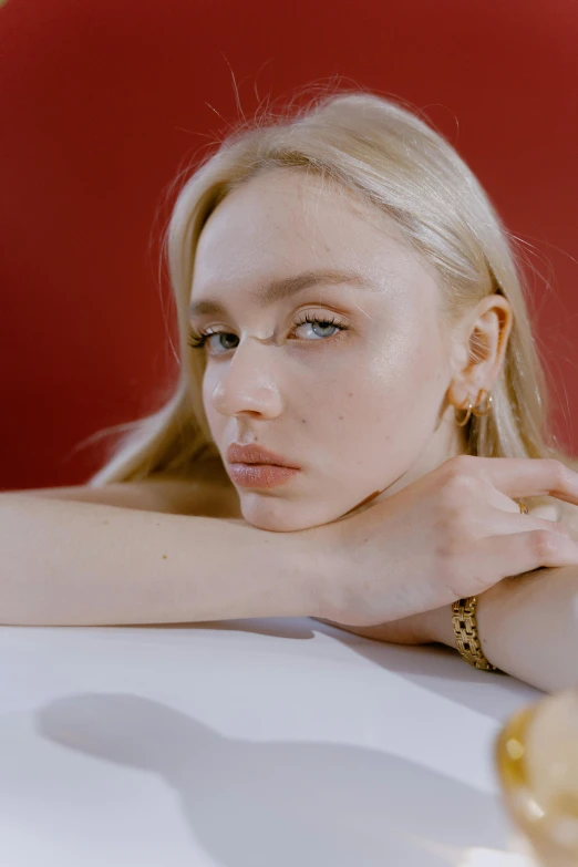 a woman sitting at a table with a glass of wine, an album cover, inspired by Elsa Bleda, trending on pexels, photorealism, gold hoop earings, albino white pale skin, sydney sweeney, gold and red metal