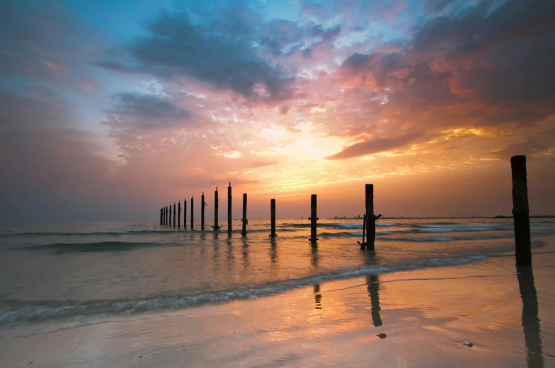 a group of poles sitting on top of a beach next to the ocean, inspired by Frederick Goodall, pexels contest winner, romanticism, sunrise colors, pillars, highly symmetrical, australian beach