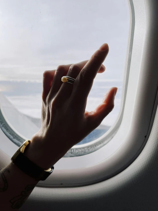 a woman's hand reaching out of an airplane window, by Lucia Peka, gold rings, right hand side profile, 🚿🗝📝, profile image