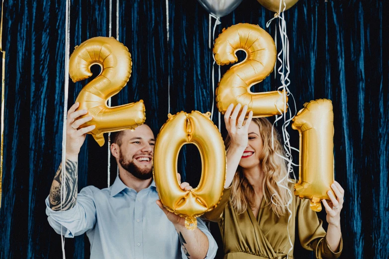 a man and woman holding up balloons that say 2021, a photo, by Julia Pishtar, trending on pexels, gold and indigo, gold linens, sydney sweeney, promotional image