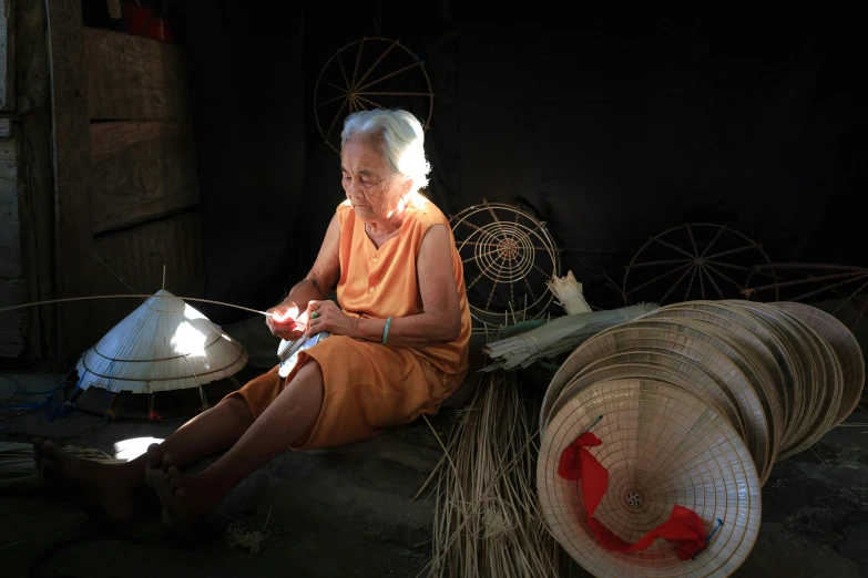 a woman sitting next to a pile of baskets, a portrait, by Ruth Jên, pexels contest winner, lighting her with a rim light, an elderly, behind the scenes, warping