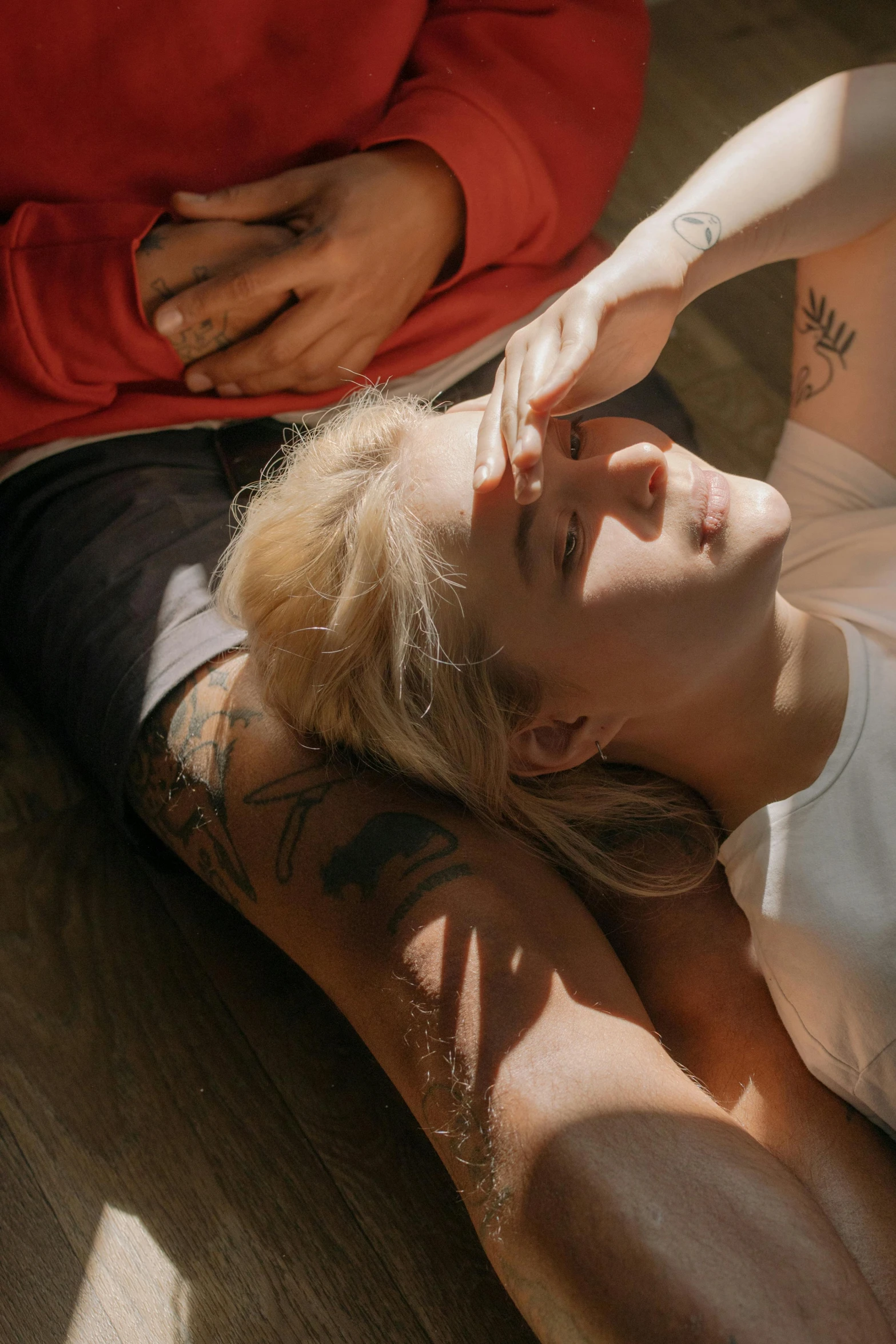 a woman laying on the ground next to a man, a tattoo, inspired by Elsa Bleda, trending on pexels, pale hair, sun overhead, lesbians, head in hands