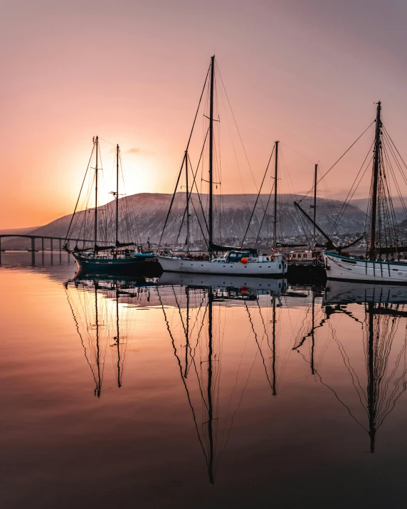 a group of boats sitting on top of a body of water, by Harald Giersing, pexels contest winner, romanticism, reykjavik junior college, warm glow, three masts, still water calm as a mirror