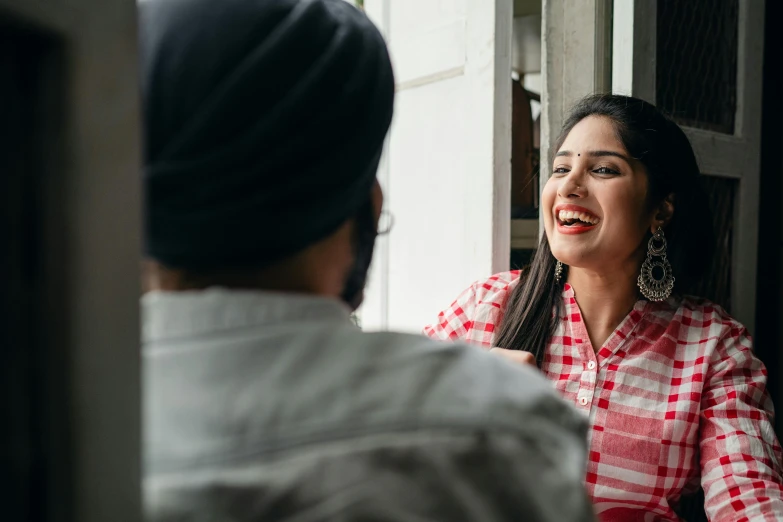 a woman in a red and white checkered shirt talking to a man in a black turban, a picture, pexels contest winner, she is smiling and excited, looking outside, promotional image, indian