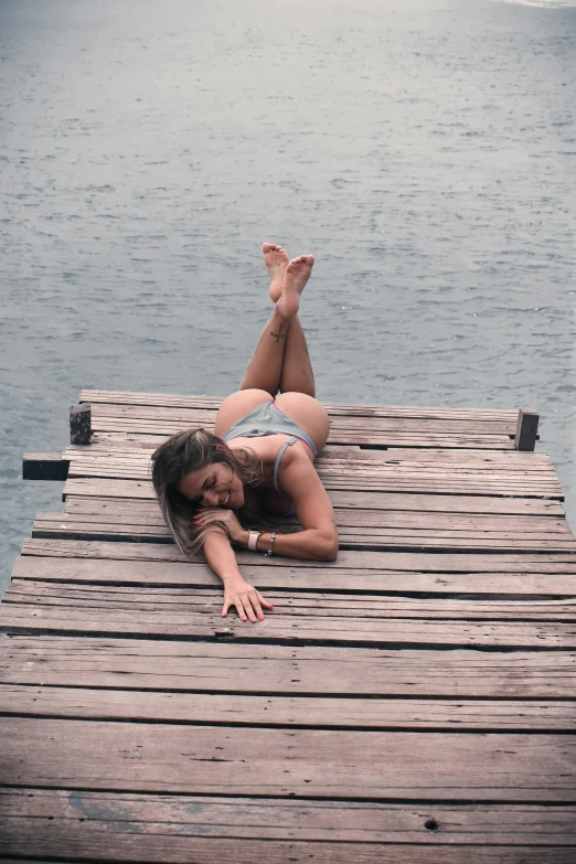 a woman laying on a dock next to a body of water, pretty face with arms and legs, posing for a picture, exposed thighs, looking down from above