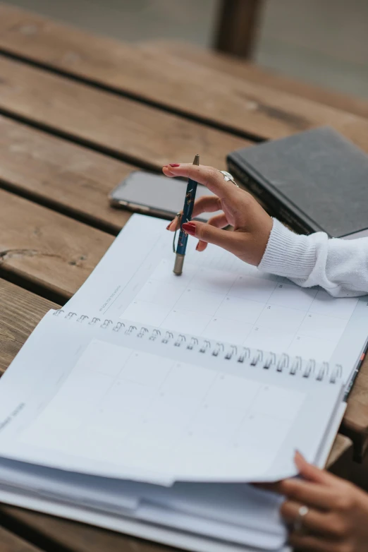 a woman sitting at a table with a notebook and pen, trending on pexels, academic art, multiple stories, phone photo, a wooden, weekly