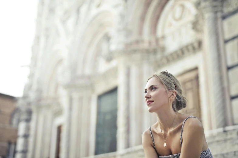 a woman sitting on the steps of a building, a picture, by Giuseppe Avanzi, pexels contest winner, renaissance, close up of a blonde woman, summer light, cathedral in the background, venice