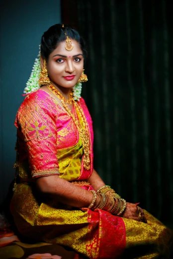 a beautiful woman sitting on top of a bed, wearing gold jewellery, with kerala motifs, with professional lighting, pink and yellow