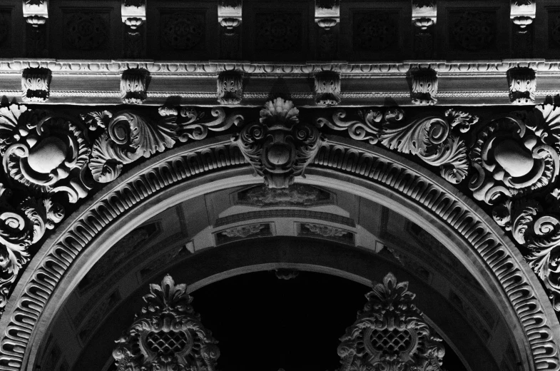 a black and white photo of a clock on a building, a black and white photo, inspired by Luis Paret y Alcazar, baroque, arched doorway, detailed faces looking up, dark and intricate photograph, carved black marble