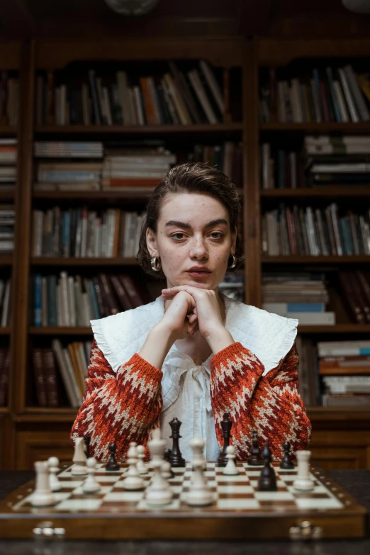 a woman sitting at a table in front of a chess board, a portrait, trending on unsplash, renaissance, maisie williams, in a library, portrait androgynous girl, wearing a fancy jacket