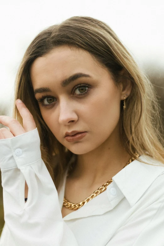 a woman wearing a white shirt and a gold chain necklace, a portrait, inspired by Emma Andijewska, trending on pexels, portrait sophie mudd, maisie williams, gold earring, portrait of vanessa morgan