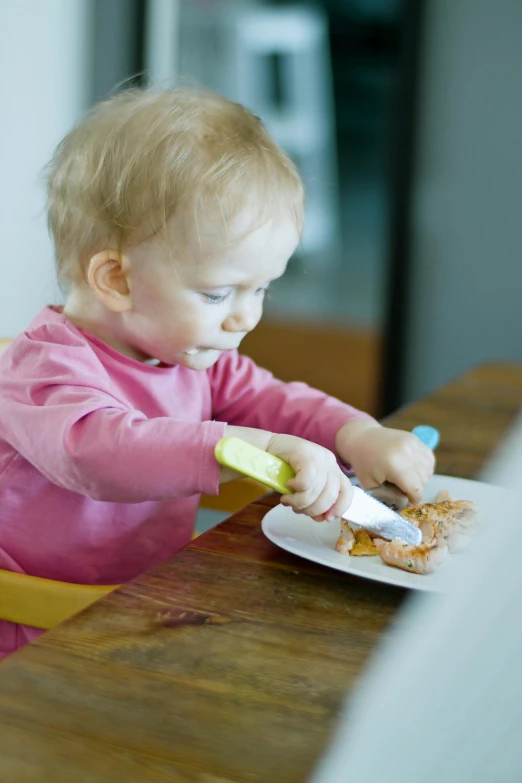 a little girl sitting at a table with a plate of food, holding a yellow toothbrush, holding a knife, manuka, bib bang