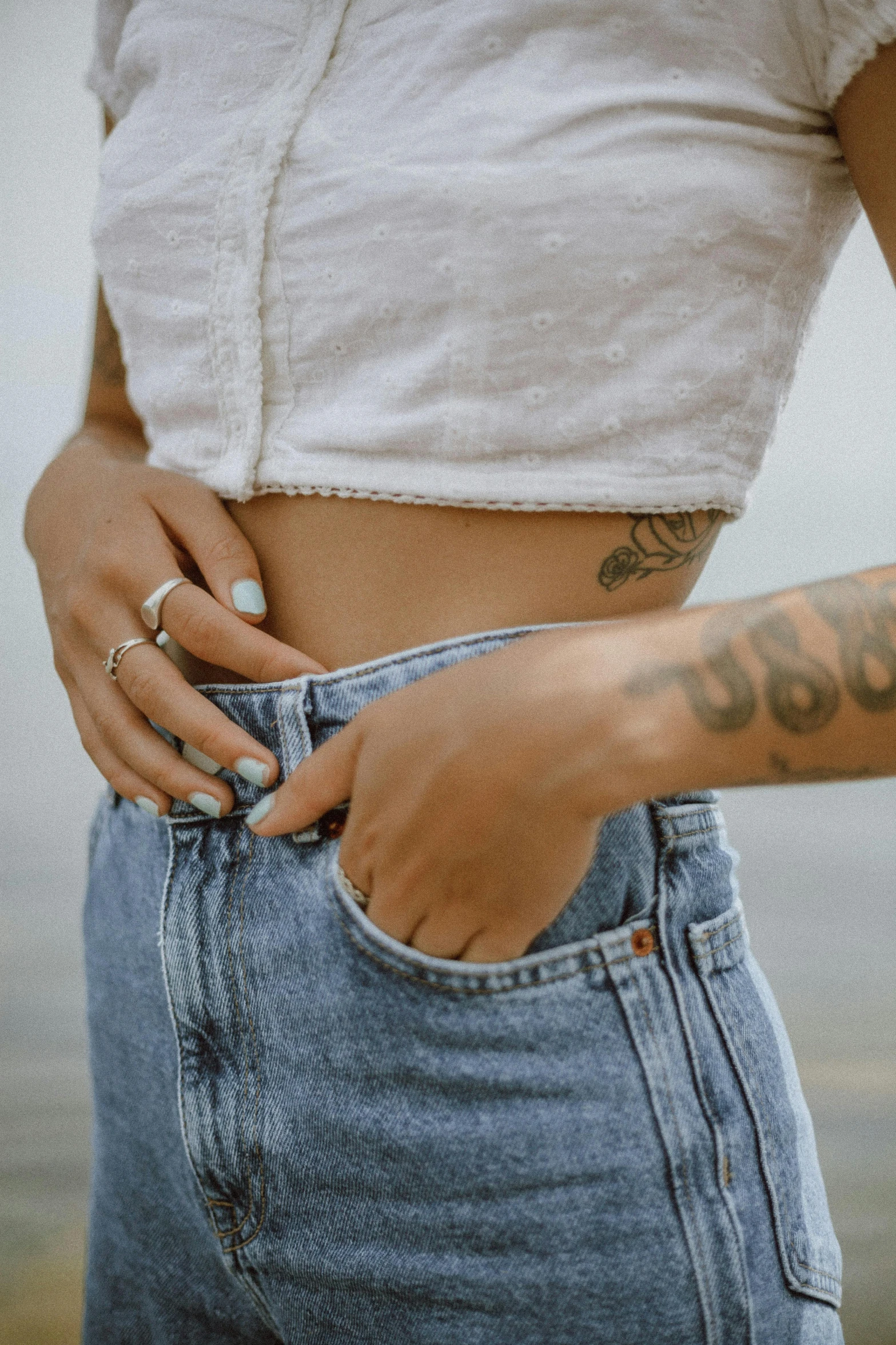 a close up of a person with a tattoo on their arm, a tattoo, inspired by Elsa Bleda, trending on pexels, physical : tinyest midriff ever, ( ( ( wearing jeans ) ) ), pastel clothing, belly free