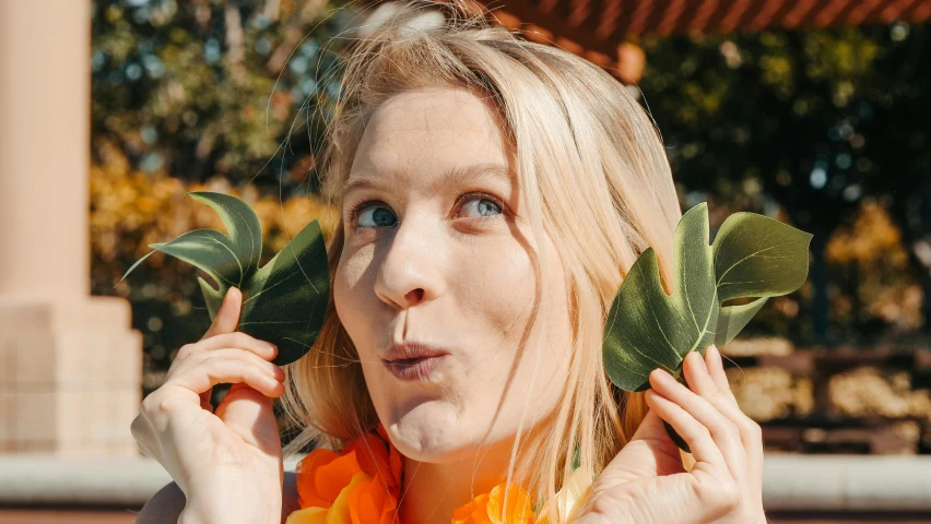 a woman holding a flower in front of her face, an album cover, pexels contest winner, kristen bell, silly playful fun face, big leaves, high quality screenshot