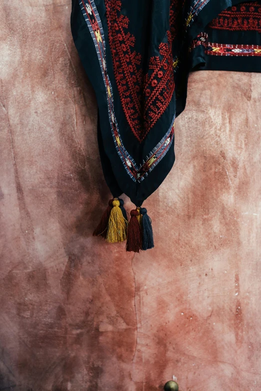 a blanket hanging on the side of a wall, by Lucia Peka, trending on unsplash, arabesque, wearing a scarf, dressing tassels gemstones, black and yellow and red scheme, decorative dark blue clothing