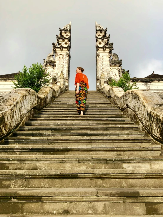 a person walking up a set of stairs, inspired by Steve McCurry, happening, javanese mythology, ancient catedral behind her, sarong, stands at the top