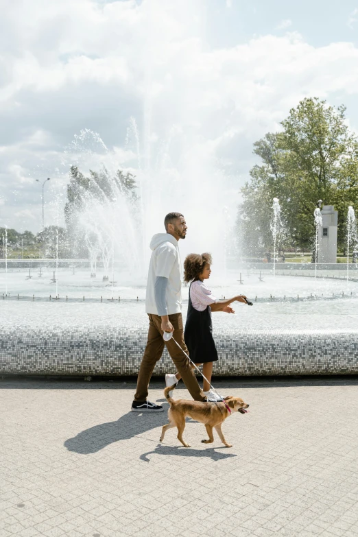 a man and woman walking a dog in front of a fountain, with a kid, 5k, warsaw, in a scenic background