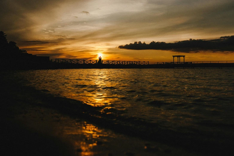 a sunset over a body of water with a bridge in the distance, pexels contest winner, happening, sunset beach, brown, medium portrait, slide show