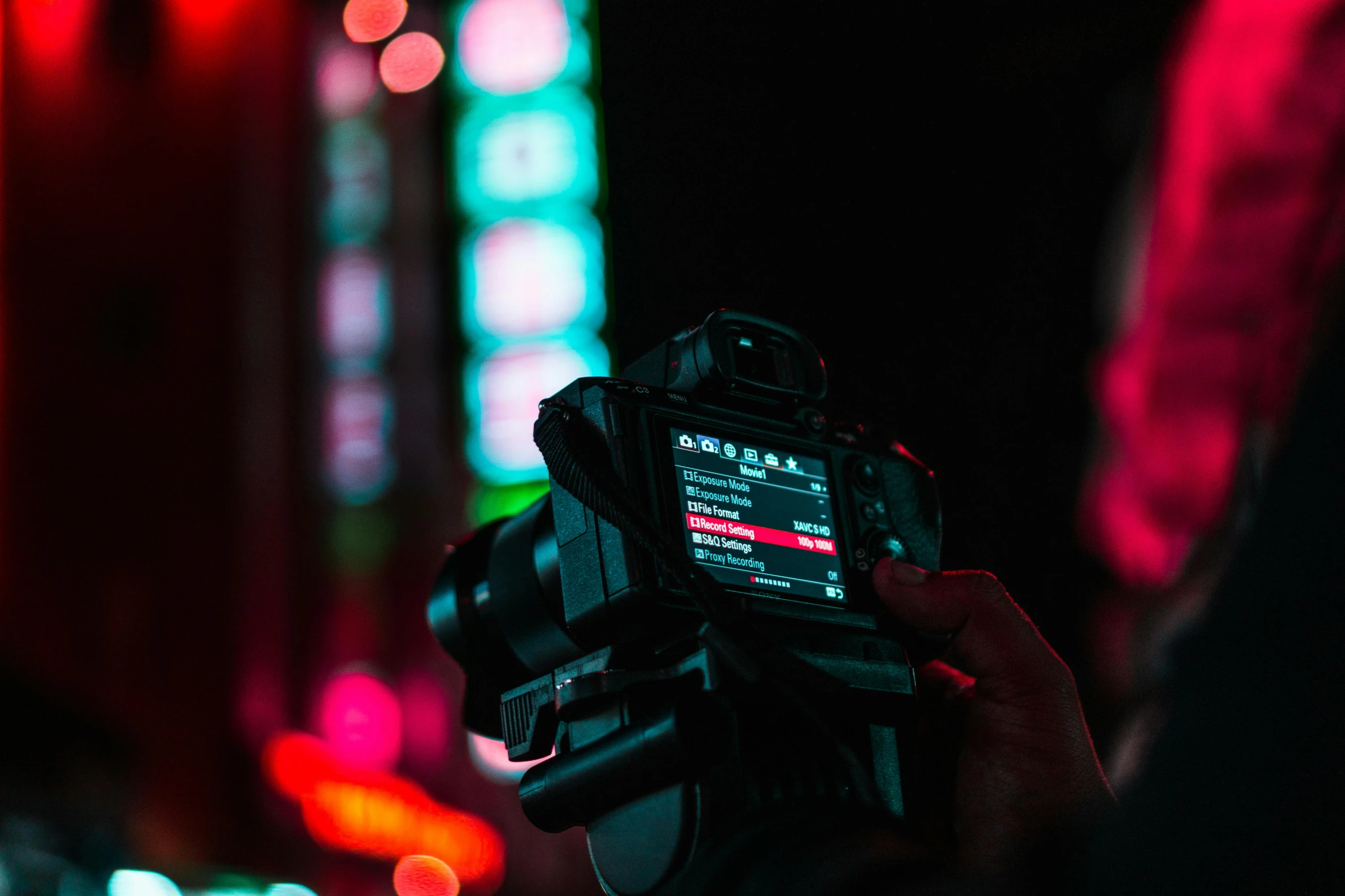 a close up of a person holding a camera, by Adam Marczyński, pexels contest winner, red neon lights inside it, instagram post, during the night, rack focus