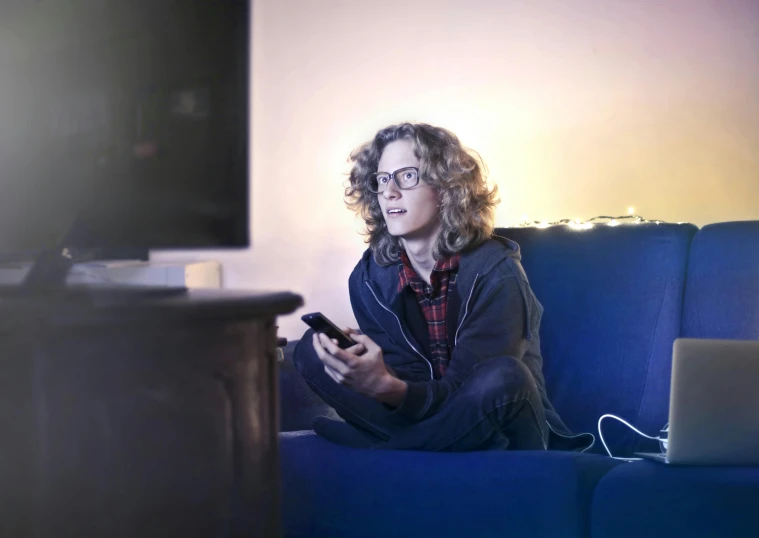 a woman sitting on a couch using a cell phone, pexels, happening, watching tv, teenage boy, lights on, androgynous male