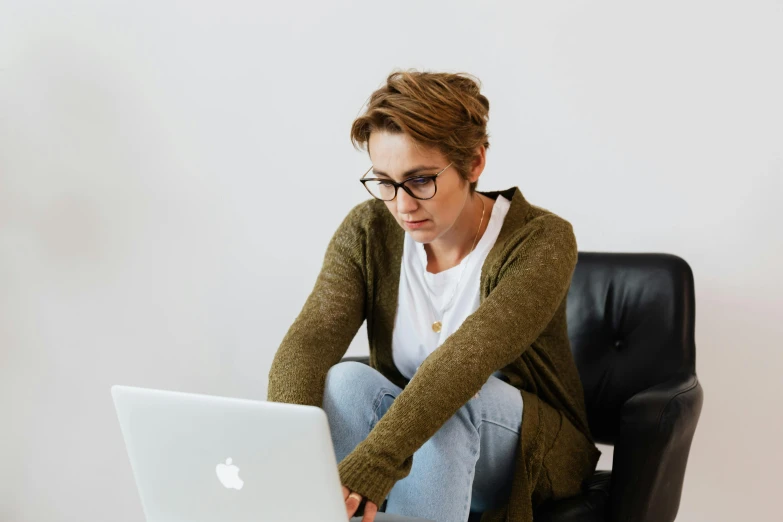 a woman sitting on a chair using a laptop, by Carey Morris, trending on pexels, wearing small round glasses, concentrated, aged 2 5, wearing elegant casual clothes