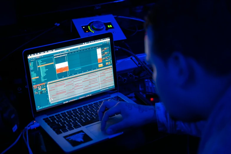 a man sitting in front of a laptop computer, by Matt Cavotta, unsplash, holography, blue and orange lighting, synthesizers, sitting at a control center, lie detector test