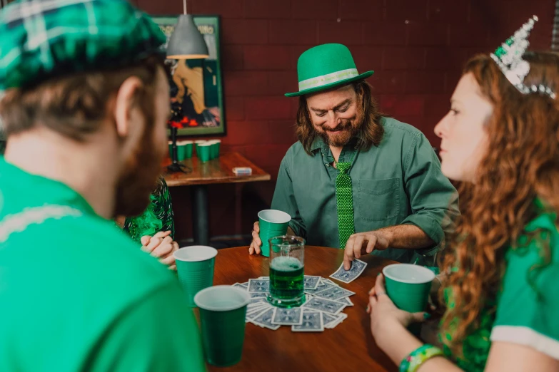 a couple of people that are sitting at a table, wearing green, wizard shuffling cards, drinks, irish