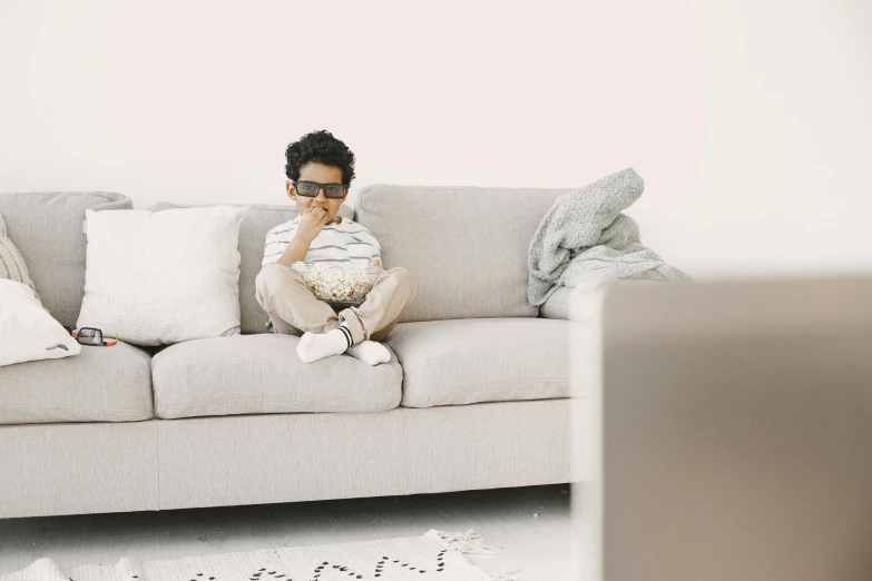 a little boy sitting on a couch holding a teddy bear, a cartoon, pexels, visual art, eating chips and watching tv, white l shaped couch, sitting in an empty white room, movie setup