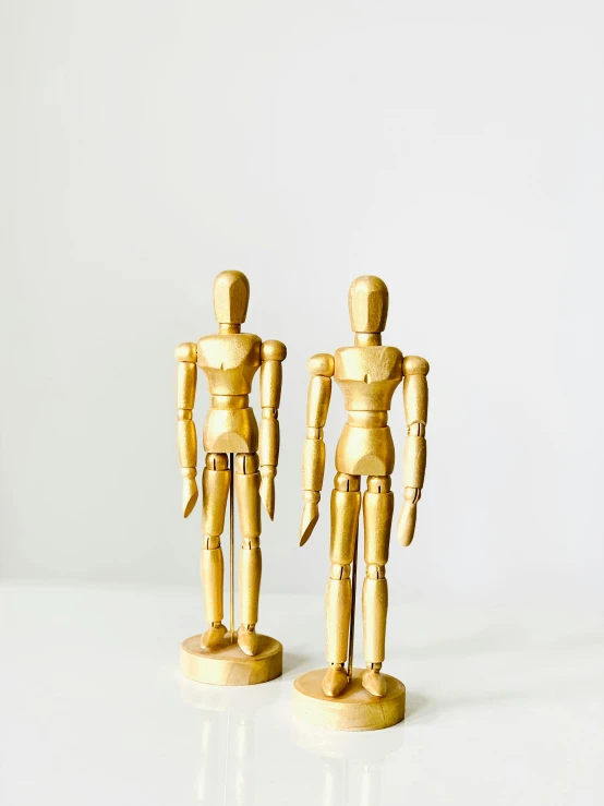 a couple of wooden figures standing next to each other, by Arabella Rankin, trending on unsplash, accented in bright metallic gold, articulated joints, 1 9 7 0 s, realistic ”