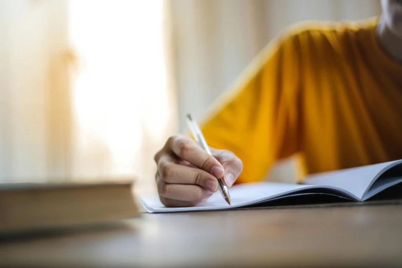 a person sitting at a table with a book and a pen, yellow, lined paper, getty images, multiple stories