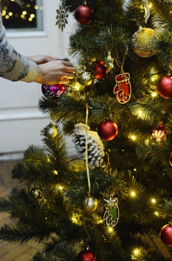 a person decorating a christmas tree with ornaments, by Alice Mason, bespoke, casually dressed, easy to use, gold trimmings
