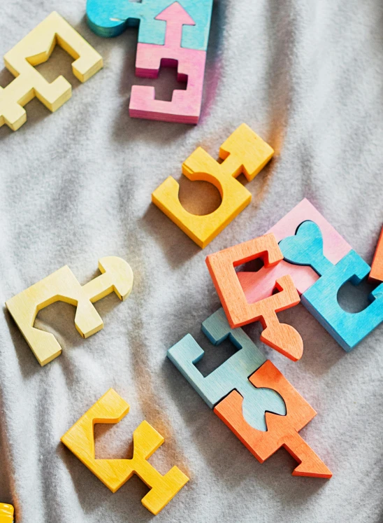 a group of wooden letters sitting on top of a bed, a jigsaw puzzle, inspired by Frederick Hammersley, letterism, bright pastel color, lesbians, menger sponge, medium close up