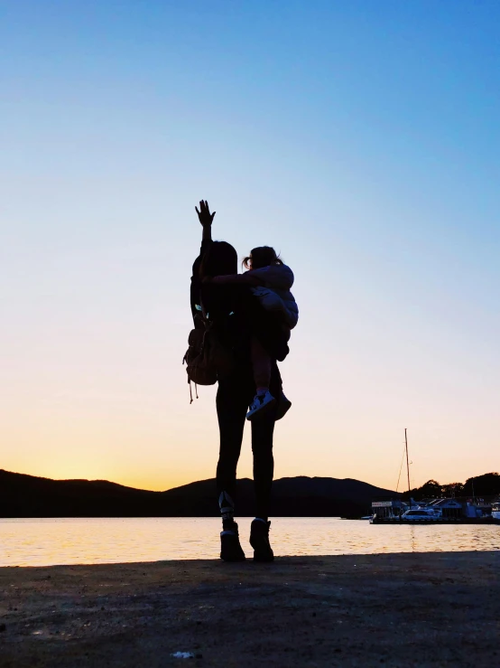 a woman standing on top of a beach next to a body of water, a man wearing a backpack, well lit sky, profile image, hands in the air