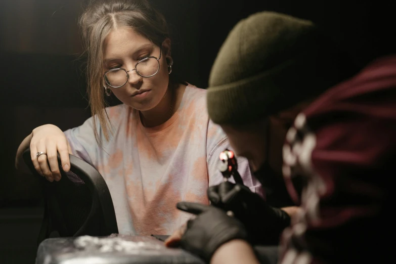 a woman getting a tattoo on a man's arm, an airbrush painting, by Lee Loughridge, trending on pexels, teenage girl, worksafe. cinematic, on a dark background, aussie baristas