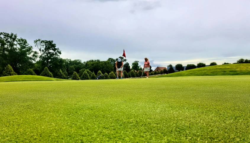 a couple of people standing on top of a green field, golf course, viewed from the ground, photo taken with provia, thumbnail