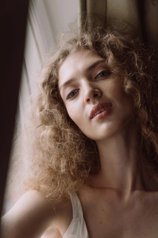 a beautiful young woman standing next to a window, inspired by Elsa Bleda, trending on pexels, renaissance, curly middle part haircut, zoomed in, video, loosely cropped