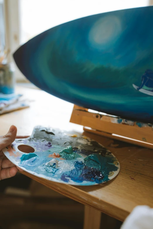 a person painting a surfboard on a table, by Elizabeth Durack, pexels contest winner, process art, warm shades of blue, painting on a badge, paua shell, painting of ornate space ship