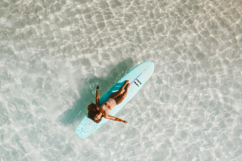 a woman laying on a surfboard in the water, pexels contest winner, brown and cyan blue color scheme, drone photograpghy, light blue skin, full body image