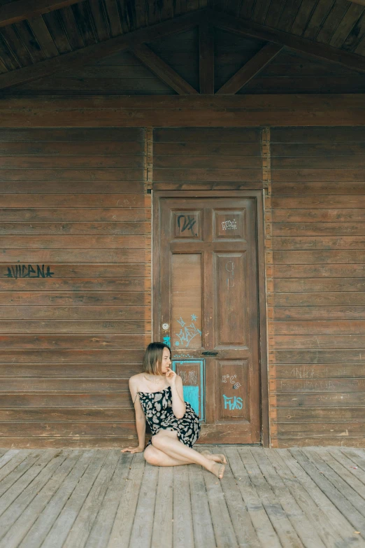 a woman sitting in front of a wooden building, inspired by Ni Yuanlu, unsplash, tall door, low quality photo, wide full body, black