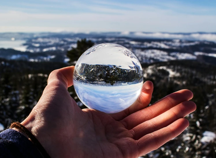 a person holding a crystal ball in their hand, by Christen Dalsgaard, unsplash contest winner, hyperrealism, wide angle landscape photography, ultra wide angle isometric view, quartz crystal, winter sun