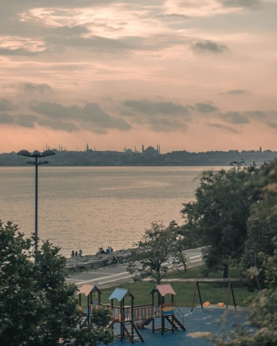 a view of a playground next to a body of water, pexels contest winner, hurufiyya, fallout style istanbul, humid evening, park in background, 🚿🗝📝