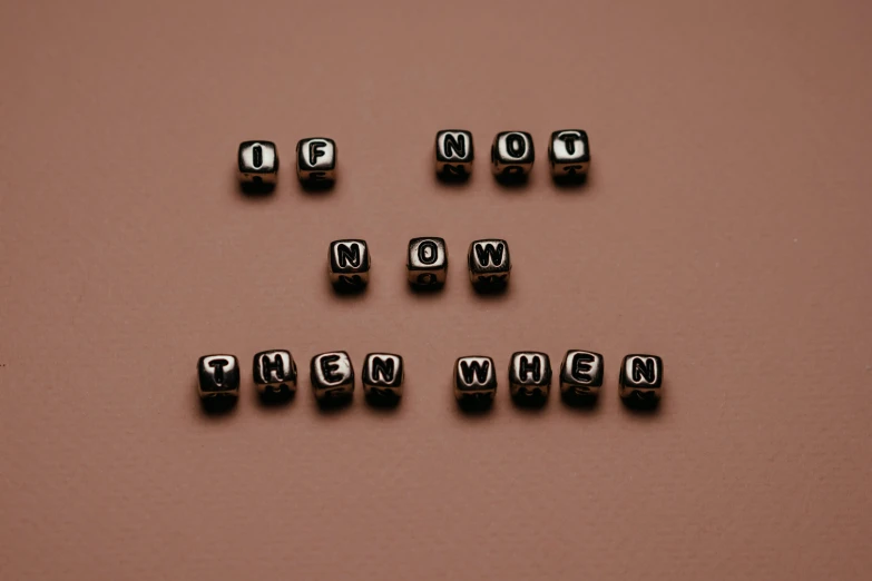 the word now spelled in black letters on a brown surface, by Nina Hamnett, unsplash, dices, life is not what it used to be, black jewellery, 'if all can begin again