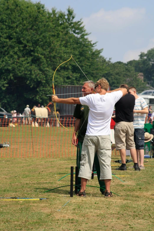 a group of people standing on top of a lush green field, archery, tournament, photograph, leisure activities