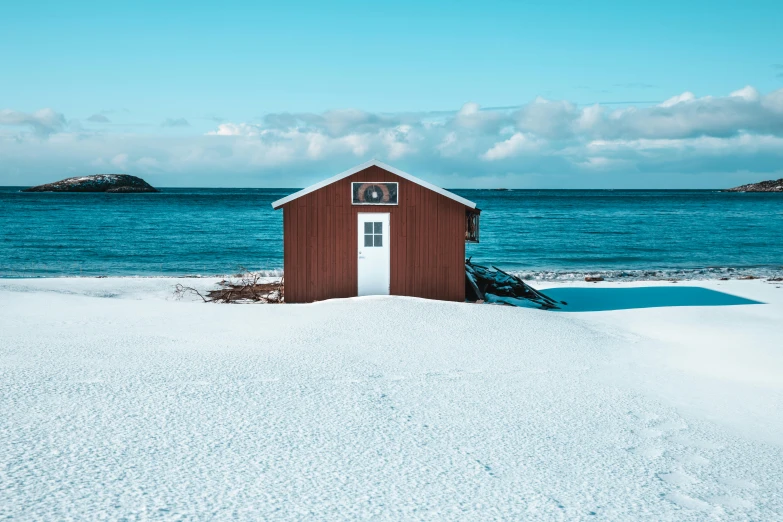 a red shed sitting on top of a snow covered beach, by Jesper Knudsen, pexels contest winner, brown and cyan blue color scheme, white building, shining sea, album cover