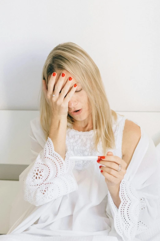 a woman sitting in bed with a thermometer in her hand, pexels, happening, crying fashion model, pregnancy, a blond, halo over her head